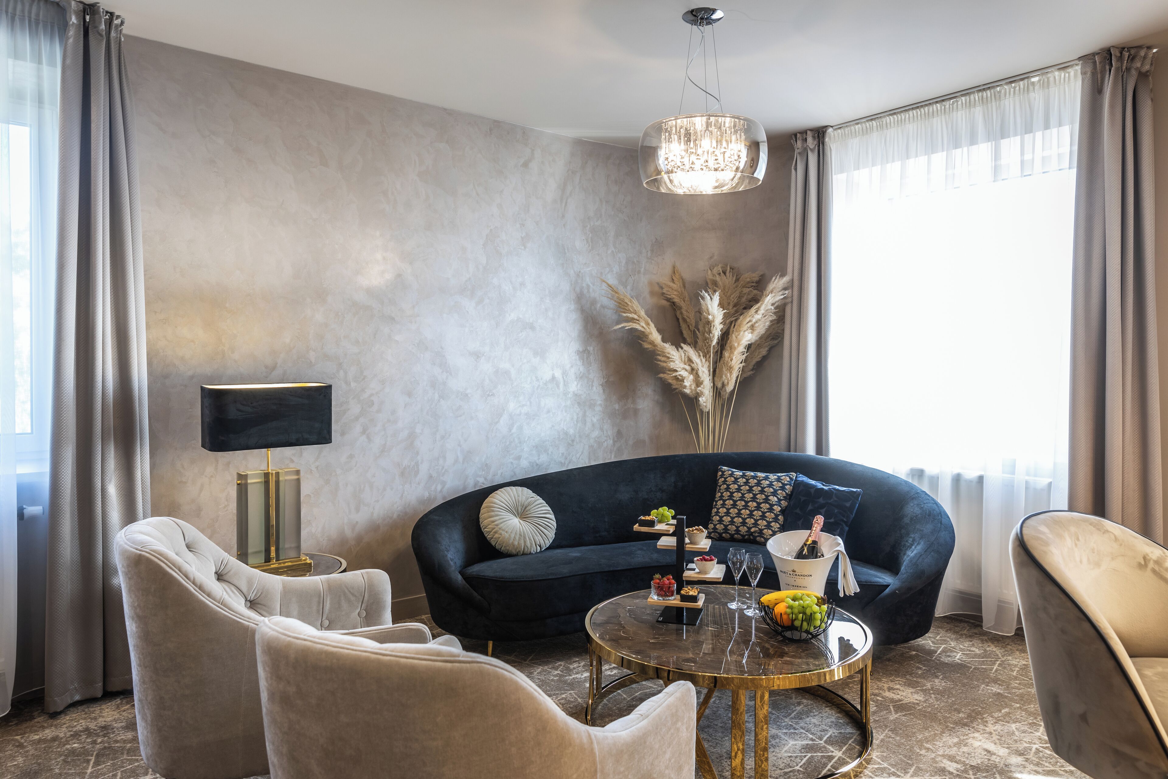 A modern living room with a dark blue sofa, a round glass coffee table, and a chandelier.