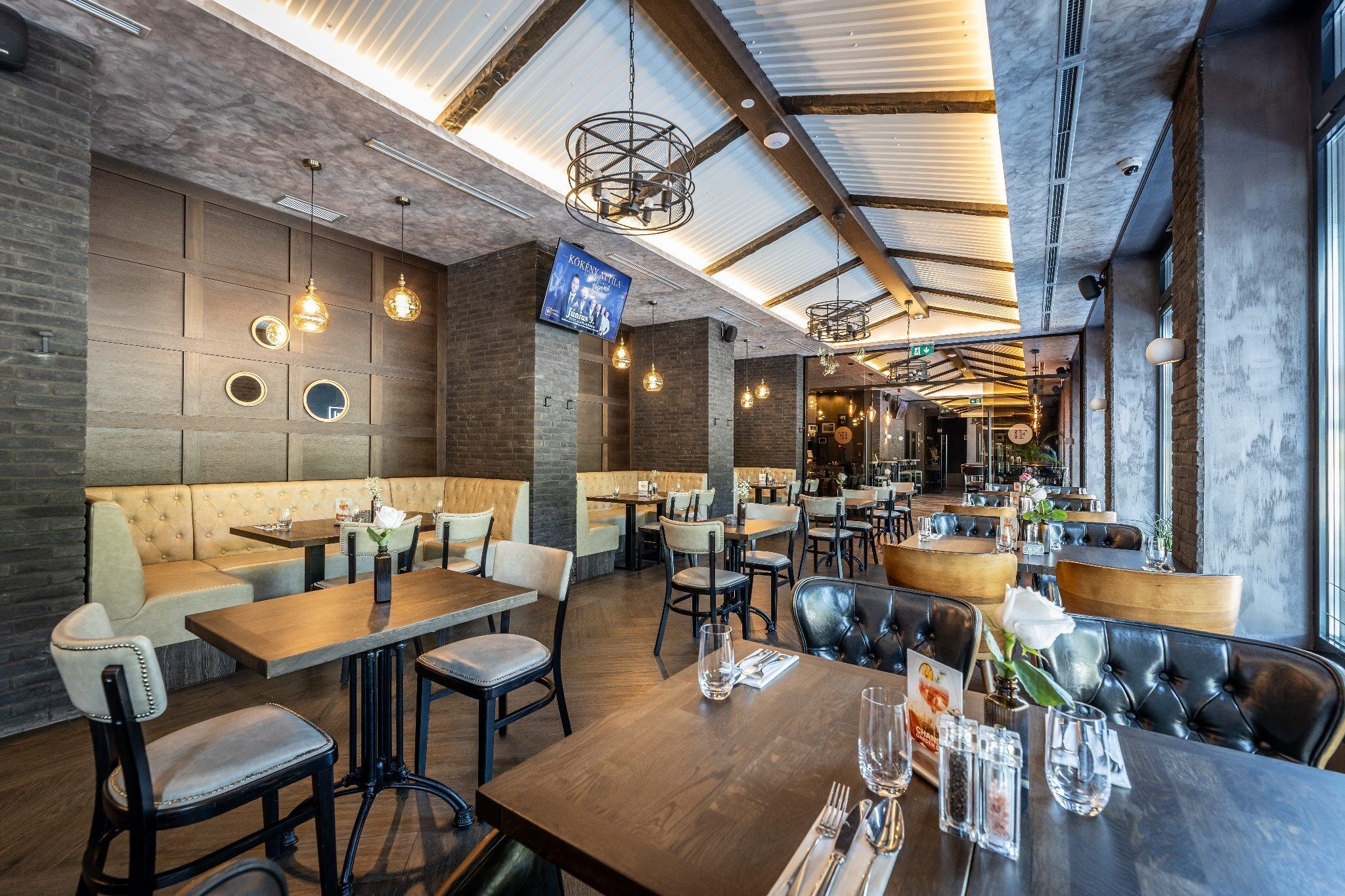 Een modern restaurantinterieur met hoge plafonds, zichtbare balken en diverse zitmogelijkheden, waaronder zitbanken en tafels.