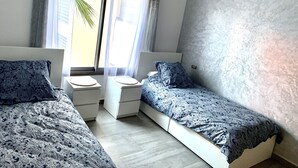 Makuuhuoneessa on kaksi sänkyä, ikkunassa läpikuultavat verhot ja seinässä kuvioitu pinta.