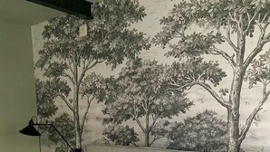 A bedroom with a bed, pillows, a lamp, and a wall mural of trees. - Rallarhustruns (Hassleholm)