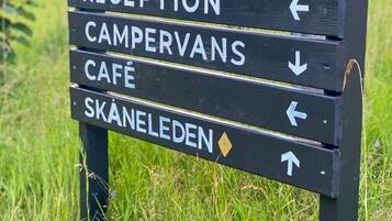En vägvisningsskylt med pilar som pekar ut olika faciliteter, inklusive parkering, rum, reception, plats för husbilar, café och Skåneleden.