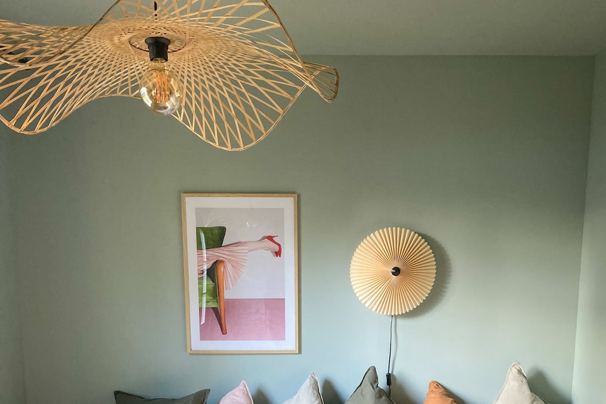 Quarto com cama, almofadas, ventoinha na parede, quadro emoldurado e dois banquinhos pretos.