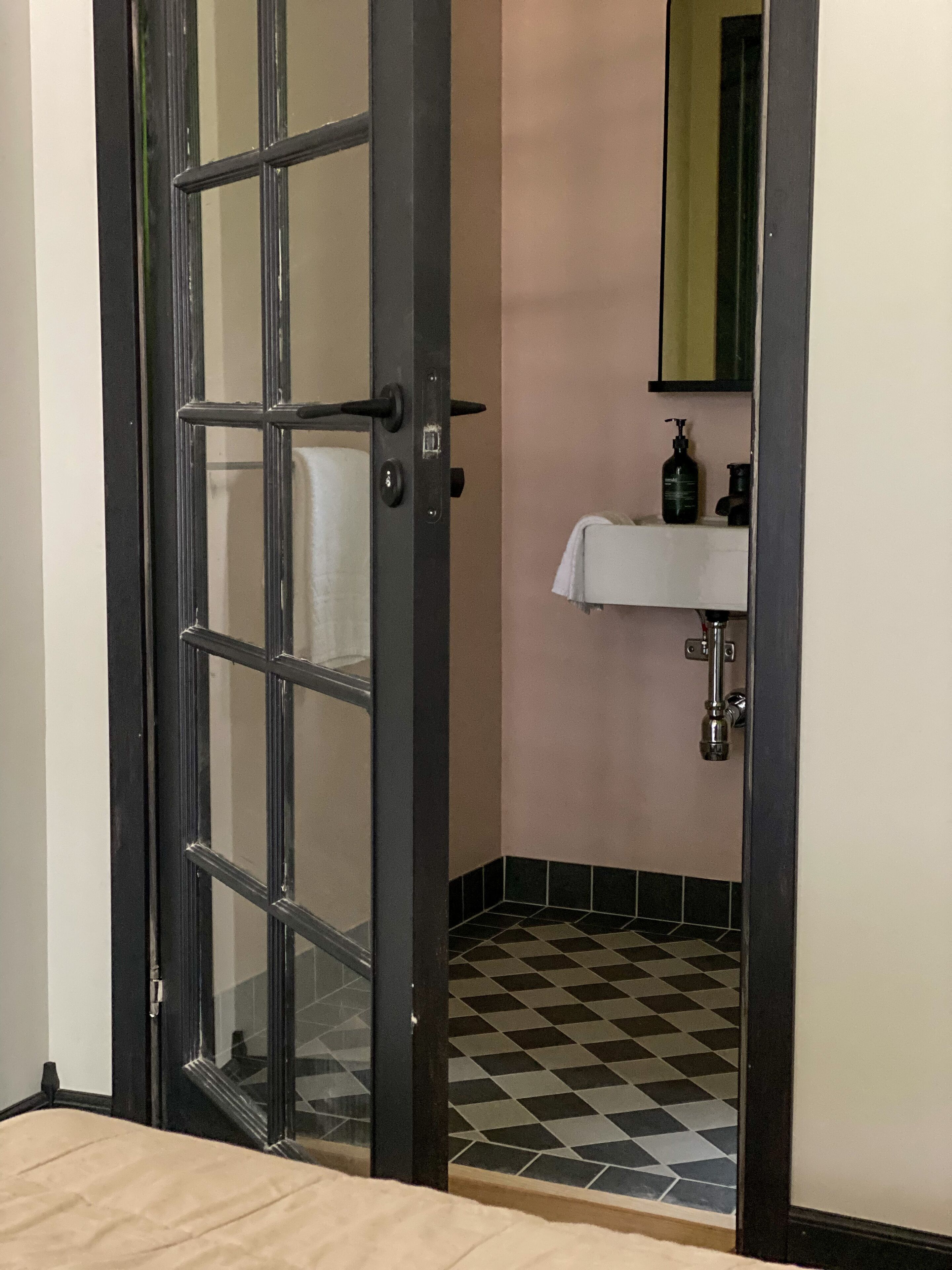 A bathroom with a checkered floor, a sink with a mirror, and a door with a handle.