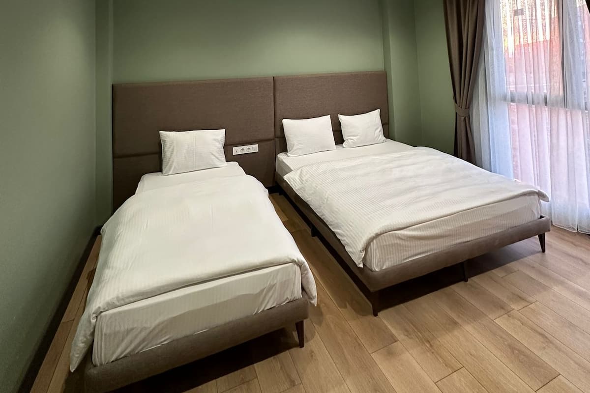 A hotel room with two beds, a large window with curtains, and recessed ceiling lights.