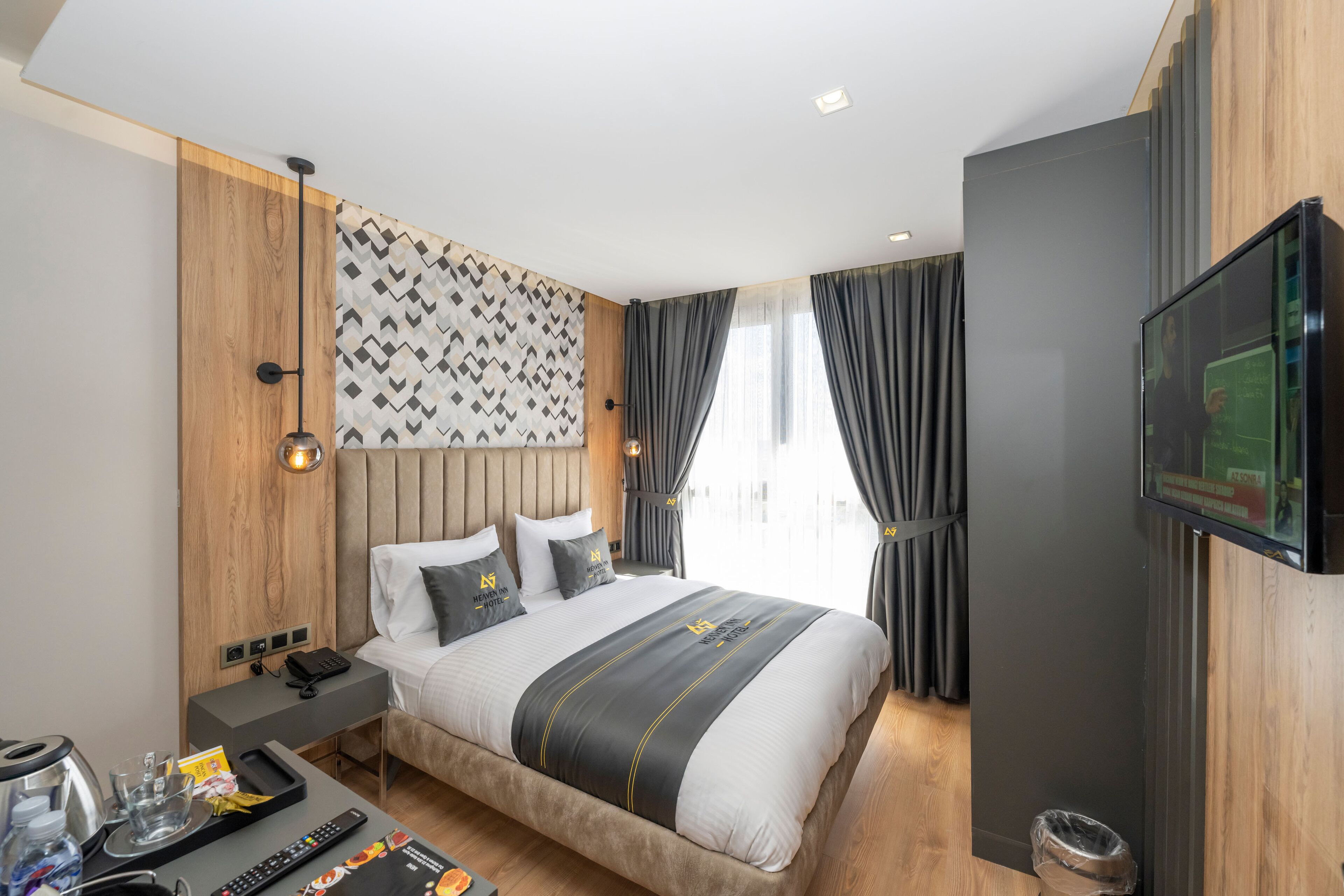 Quarto de hotel moderno com uma cama grande, uma TV de tela plana, uma mesa de cabeceira com telefone e uma TV fixada na parede.