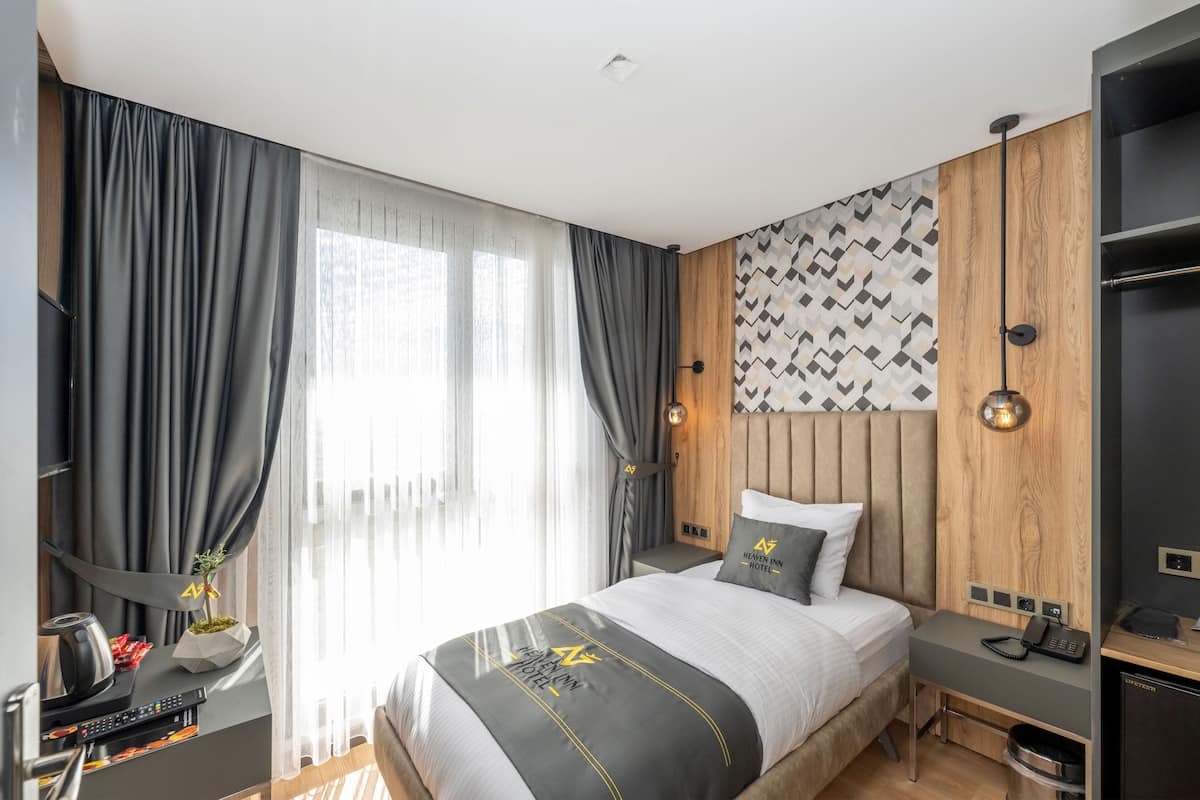 A modern hotel room with a large bed, a desk, and a wardrobe.