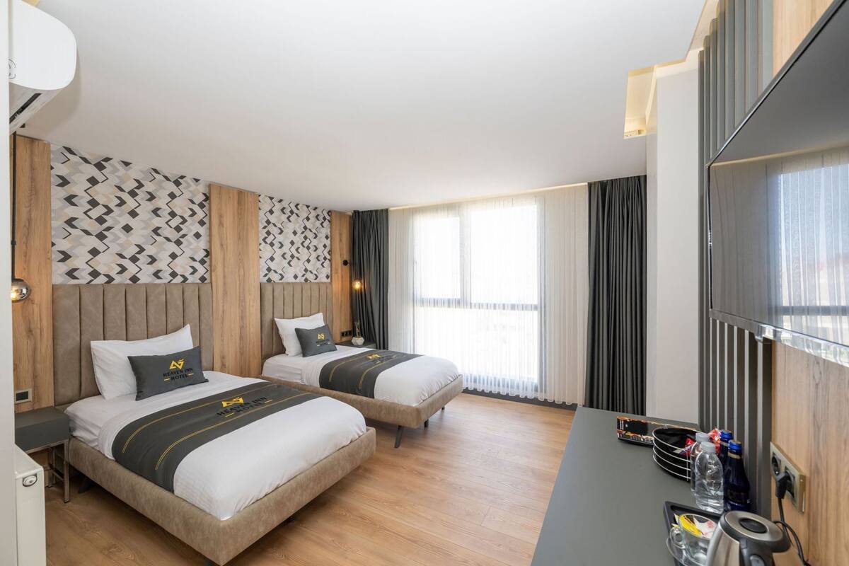 A hotel room with two beds, a desk, a TV, and a window with curtains.