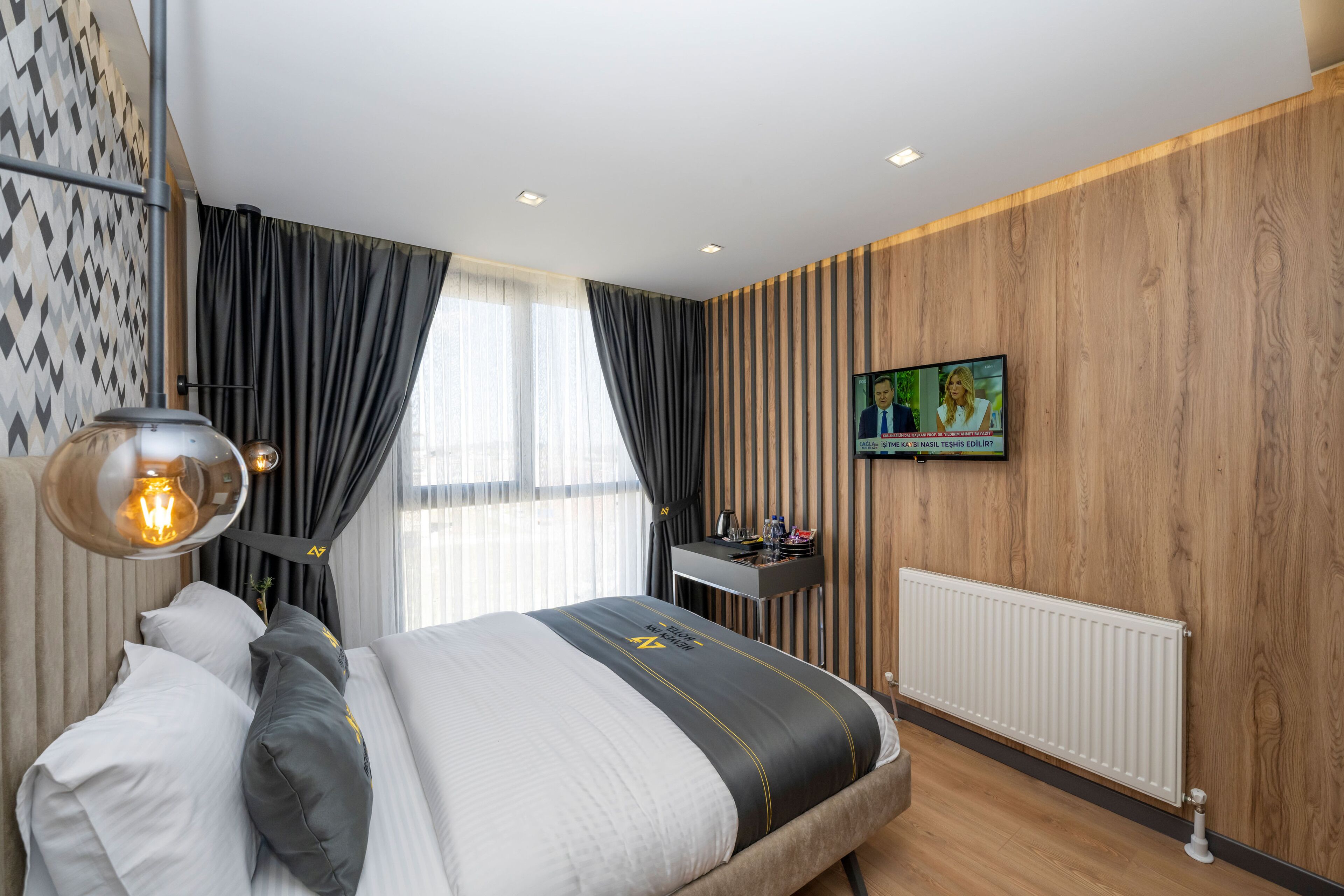 A modern hotel room with a bed, a desk, a television, and a window with curtains.