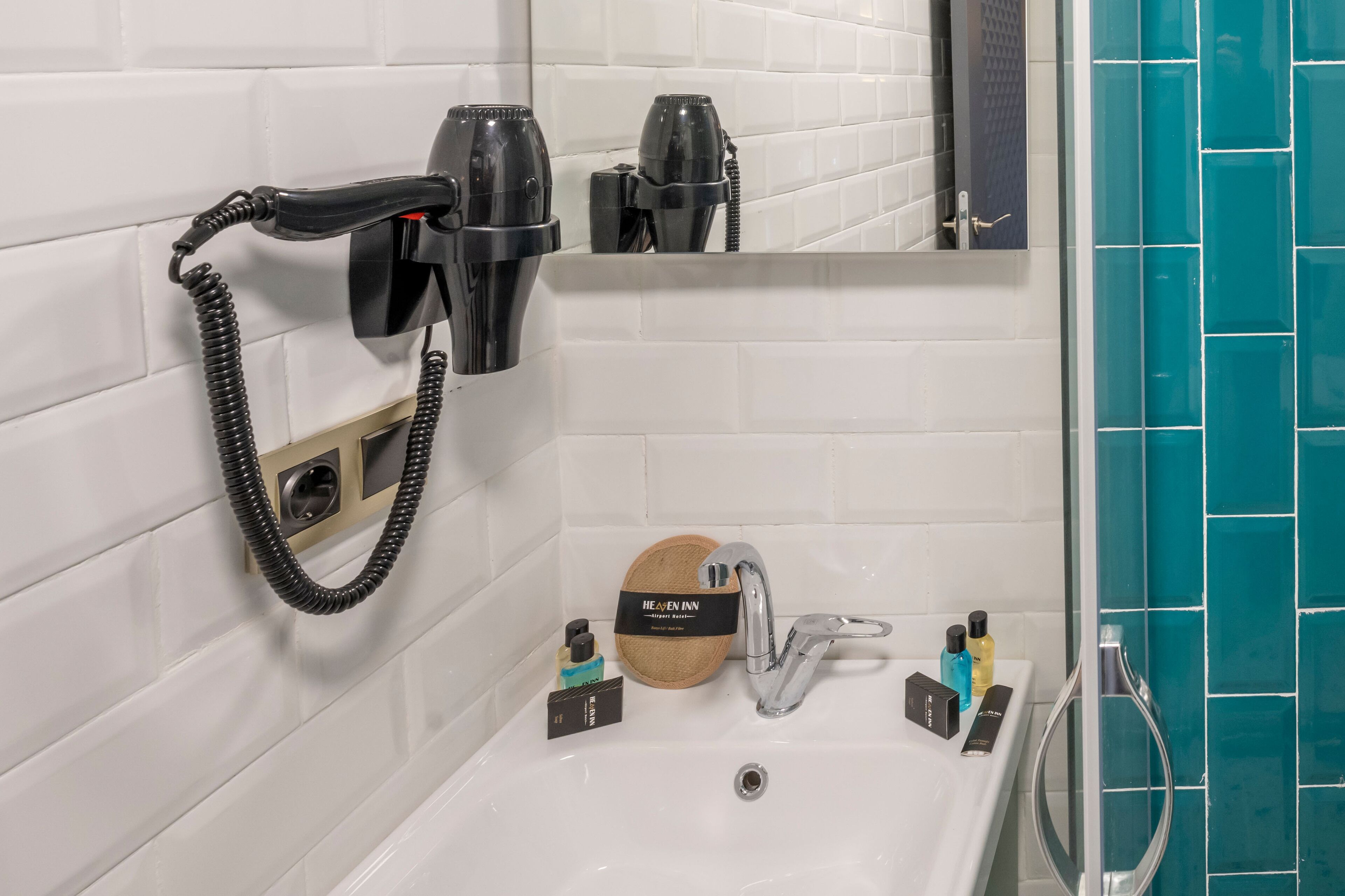 Un baño con pared de azulejos blancos, un lavabo con espejo, un secador de pelo y un perchero para toallas.