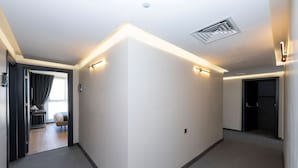 A hallway with a carpeted floor, a door on the left, and a bed visible through a window. - Heaven Inn Airport Hotel (Arnavutköy)