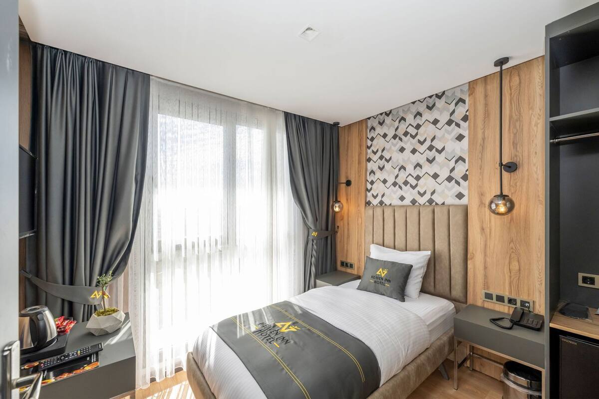 A modern hotel room with a bed, a desk with a computer, and a wall-mounted TV.
