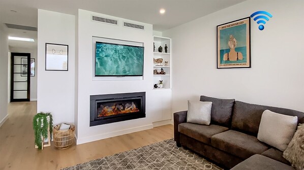 Un salon moderne avec une cheminée, un grand téléviseur à écran plat et un tableau encadré au mur.
