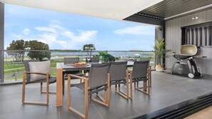 Un espace repas extérieur moderne avec vue sur la mer, un barbecue et une plante en pot.