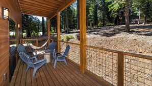A wooden deck with chairs and a table, surrounded by a wooden fence and trees. - Pine Cone Place_Brand New Build, EV Charger, Hydronic Heat, Steam Shower, 500G Wifi, Arcade & PS4 (Truckee)