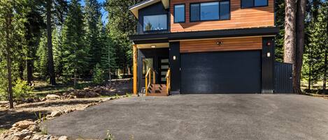 A modern two-story house with a garage, surrounded by a forest.