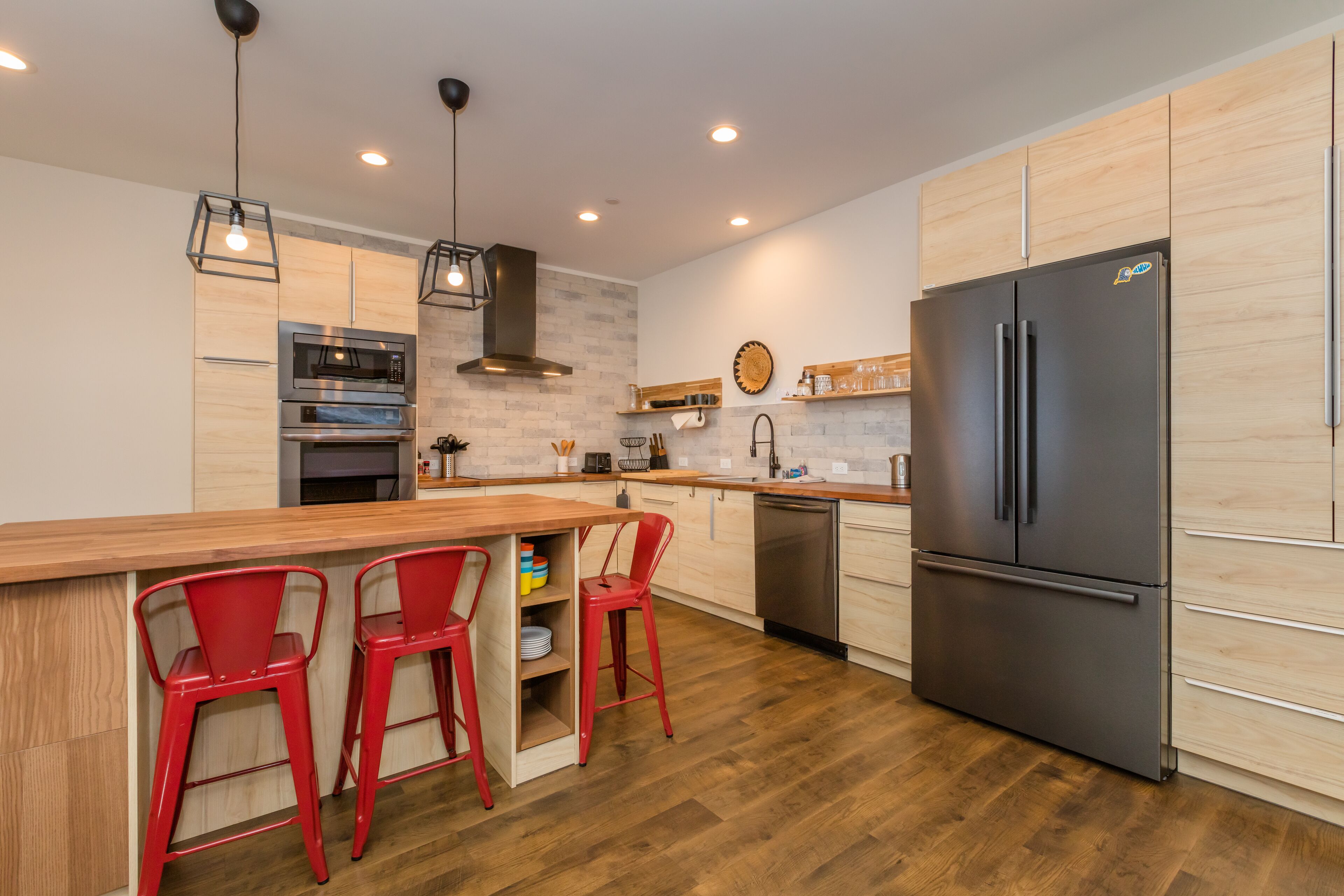 Una cocina moderna con armarios de madera, un refrigerador de acero inoxidable y taburetes rojos.
