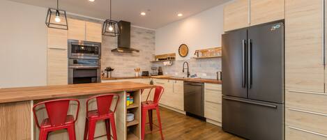 Una cocina moderna con armarios de madera, un refrigerador de acero inoxidable y taburetes rojos.