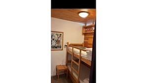 A bunk bed room with a poster on the wall, a small wooden table, and a ceiling light. - Vars: Very pretty mountain apartment. (Vars)