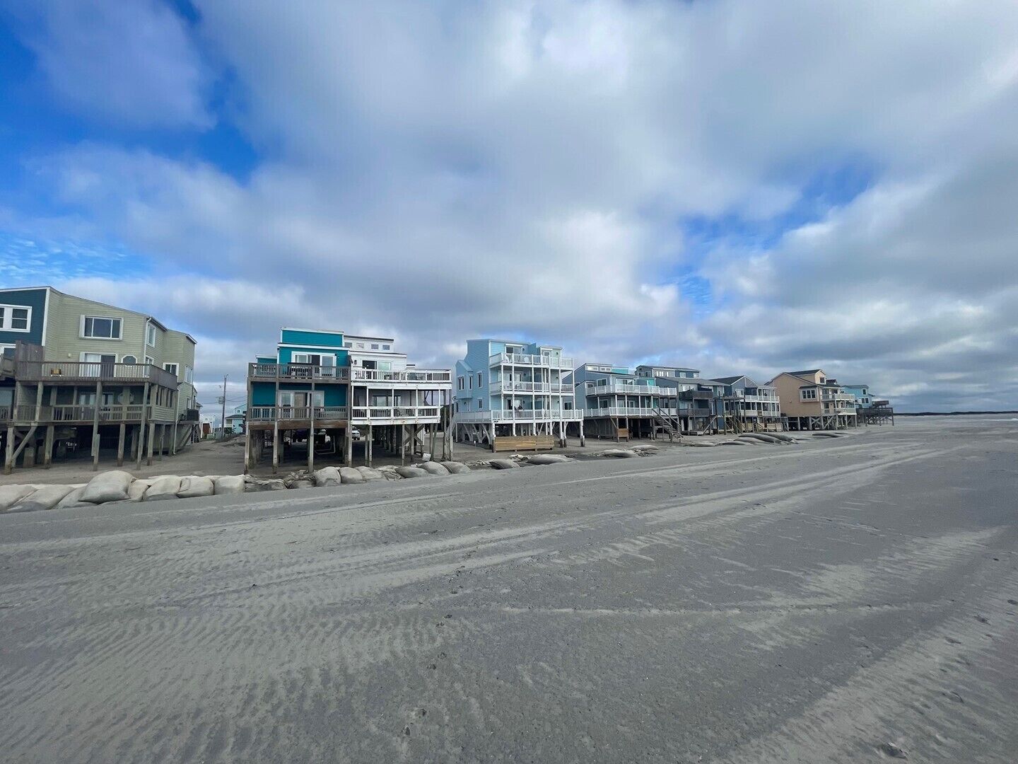 Una propiedad frente a la playa con varias construcciones, algunas elevadas sobre pilotes, y una playa arenosa al frente.