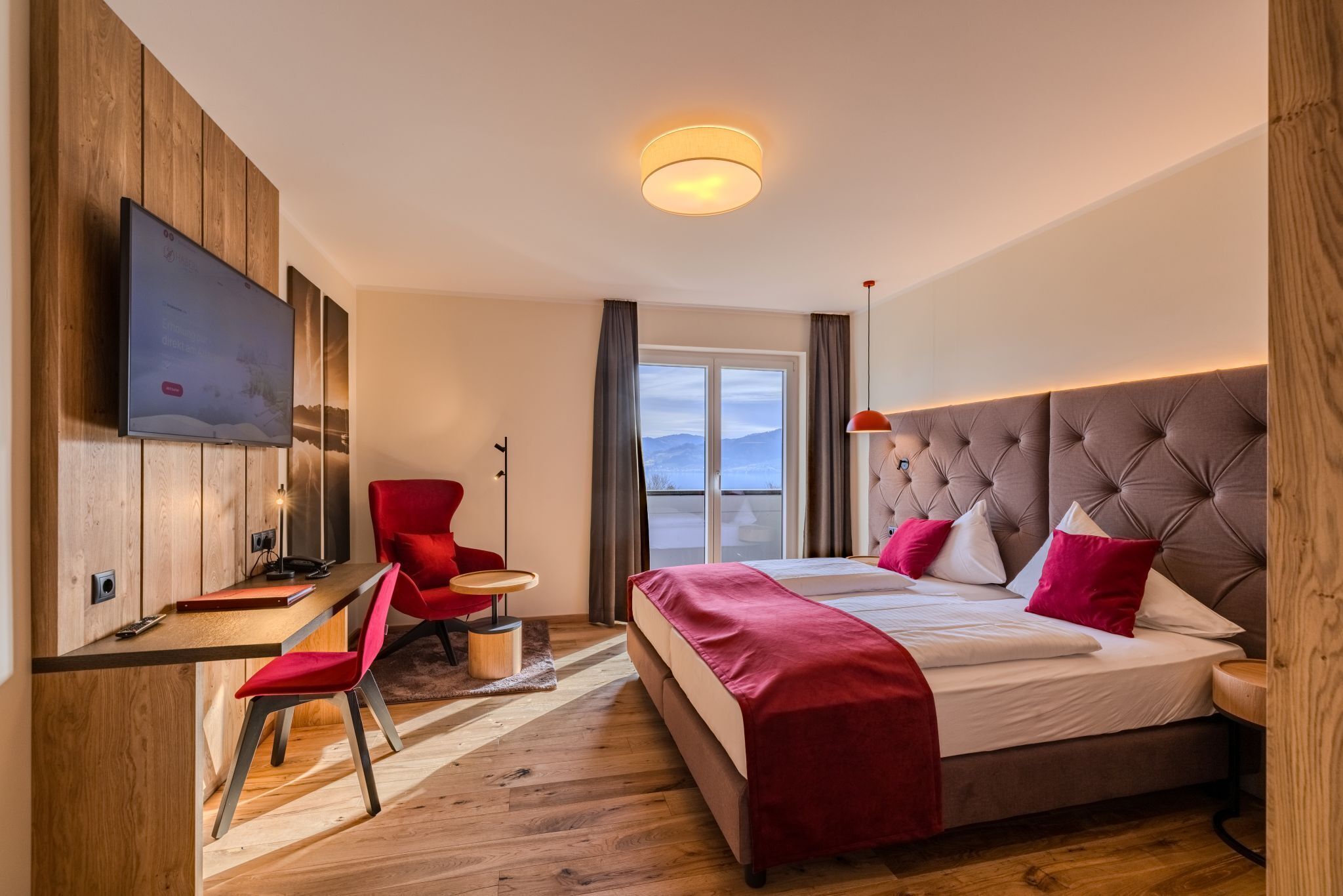 A modern hotel room with a bed, a desk, a chair, a TV, and a large window.
