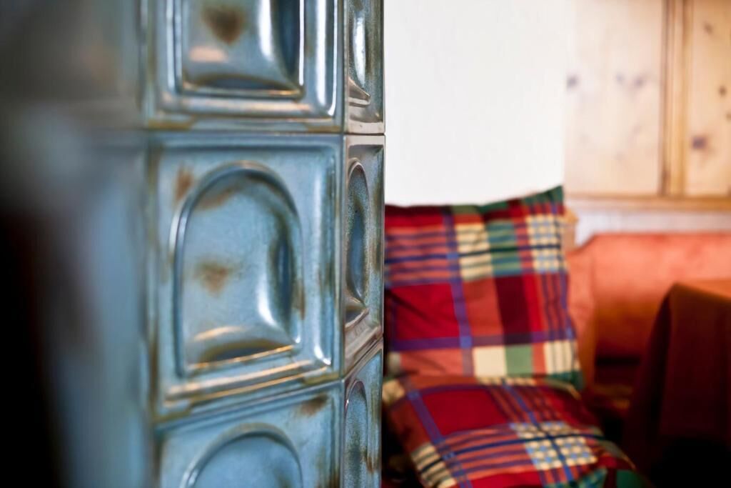 Gros plan d’un mur métallique à la texture particulière, avec un canapé et, en arrière-plan, un coussin à carreaux.