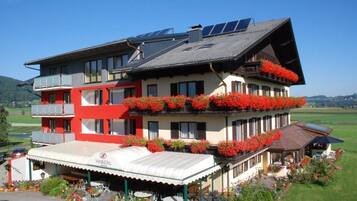 Un hotel de dos plantas con fachada roja y blanca, varios balcones con flores rojas y paneles solares en el techo.