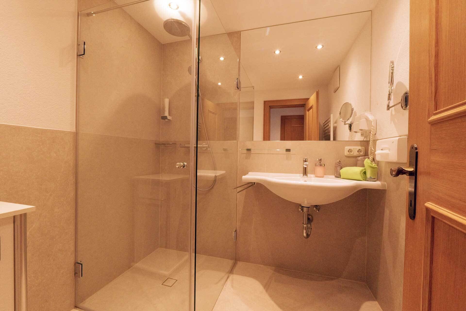 A modern bathroom with a glass shower enclosure, a sink with a mirror, and a wooden door.