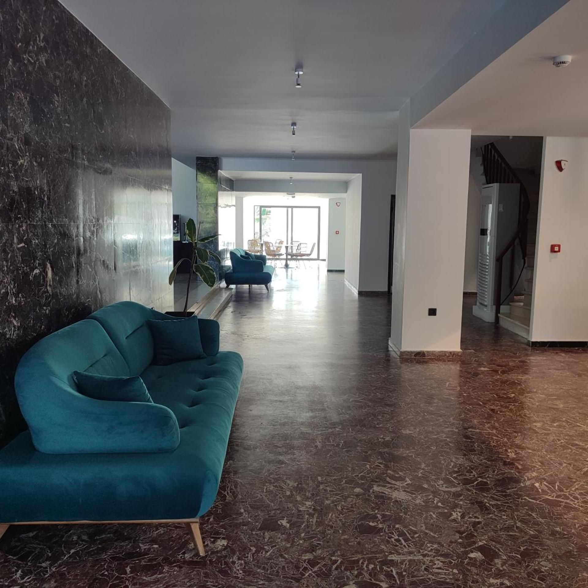 A spacious living area with a teal sofa, a large window, and a marble floor.