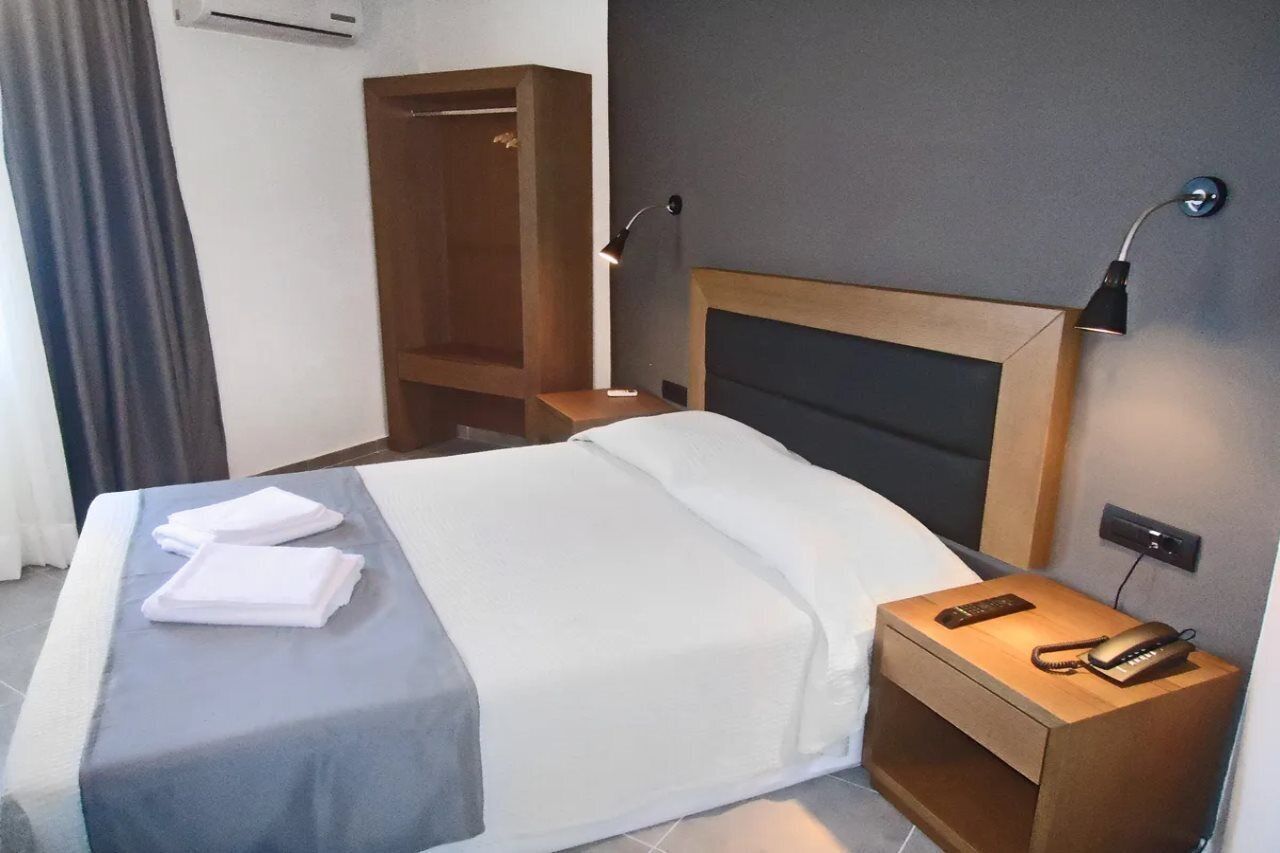 A hotel room with a bed, bedside tables, a wardrobe, and a wall-mounted phone.