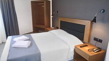 A hotel room with a bed, bedside tables, a wardrobe, and a wall-mounted phone.