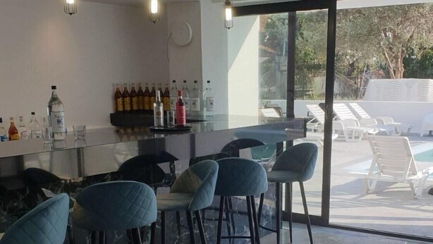 Zona de bar moderna con encimera de mármol y sillas azules, ventanas amplias con vista a la terraza, e iluminación colgante.