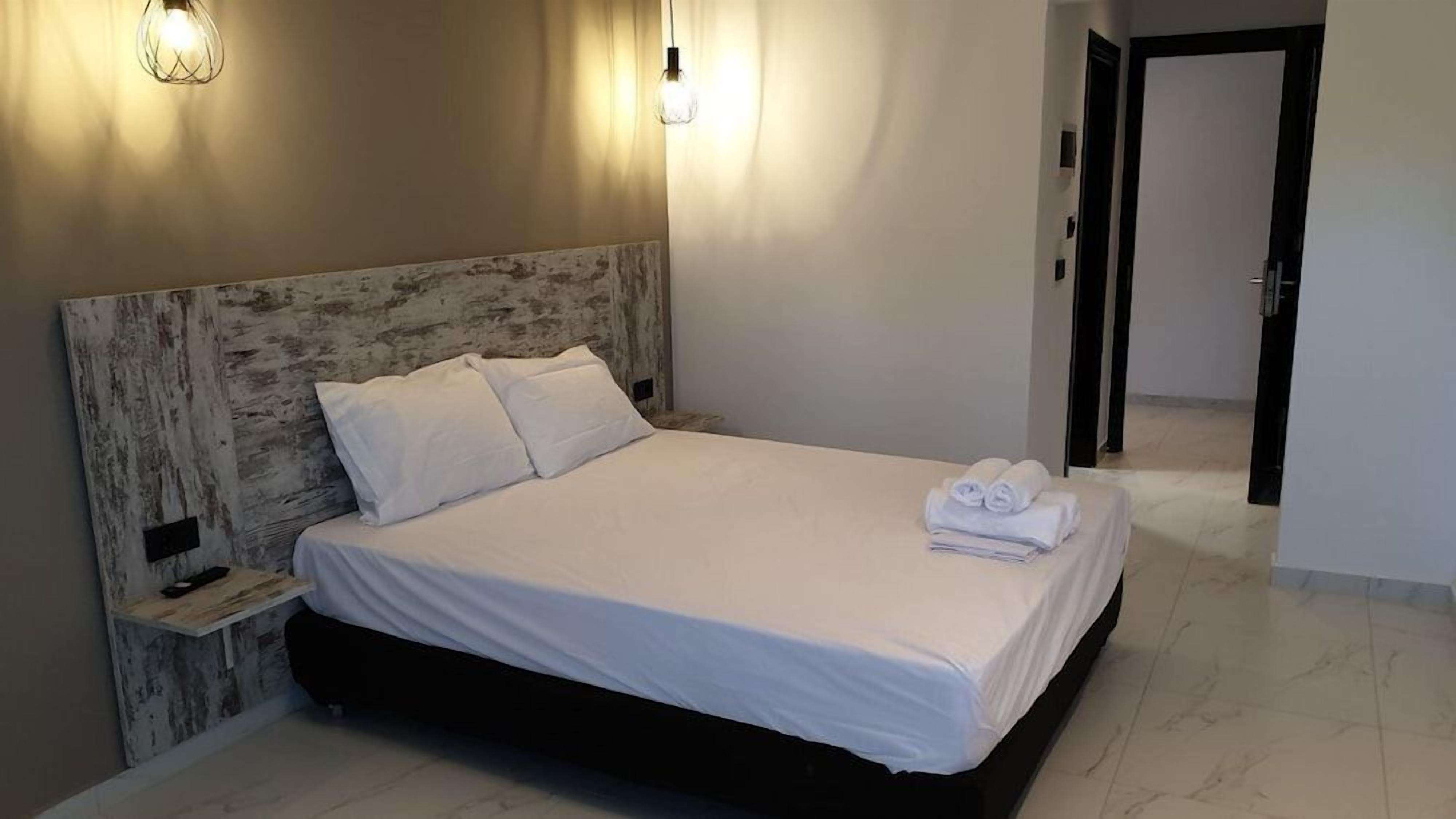 Un letto rifatto con lenzuola bianche, una testiera in legno e lampade ai lati del letto.