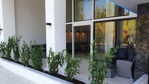 Un edificio moderno con amplios ventanales, mesas al aire libre y un jardín con plantas.