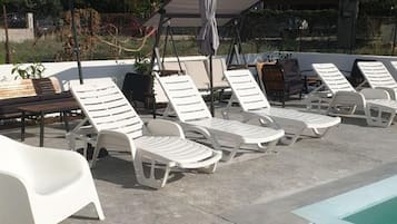 A poolside area with white lounge chairs and umbrellas, a concrete floor, and a building in the background.