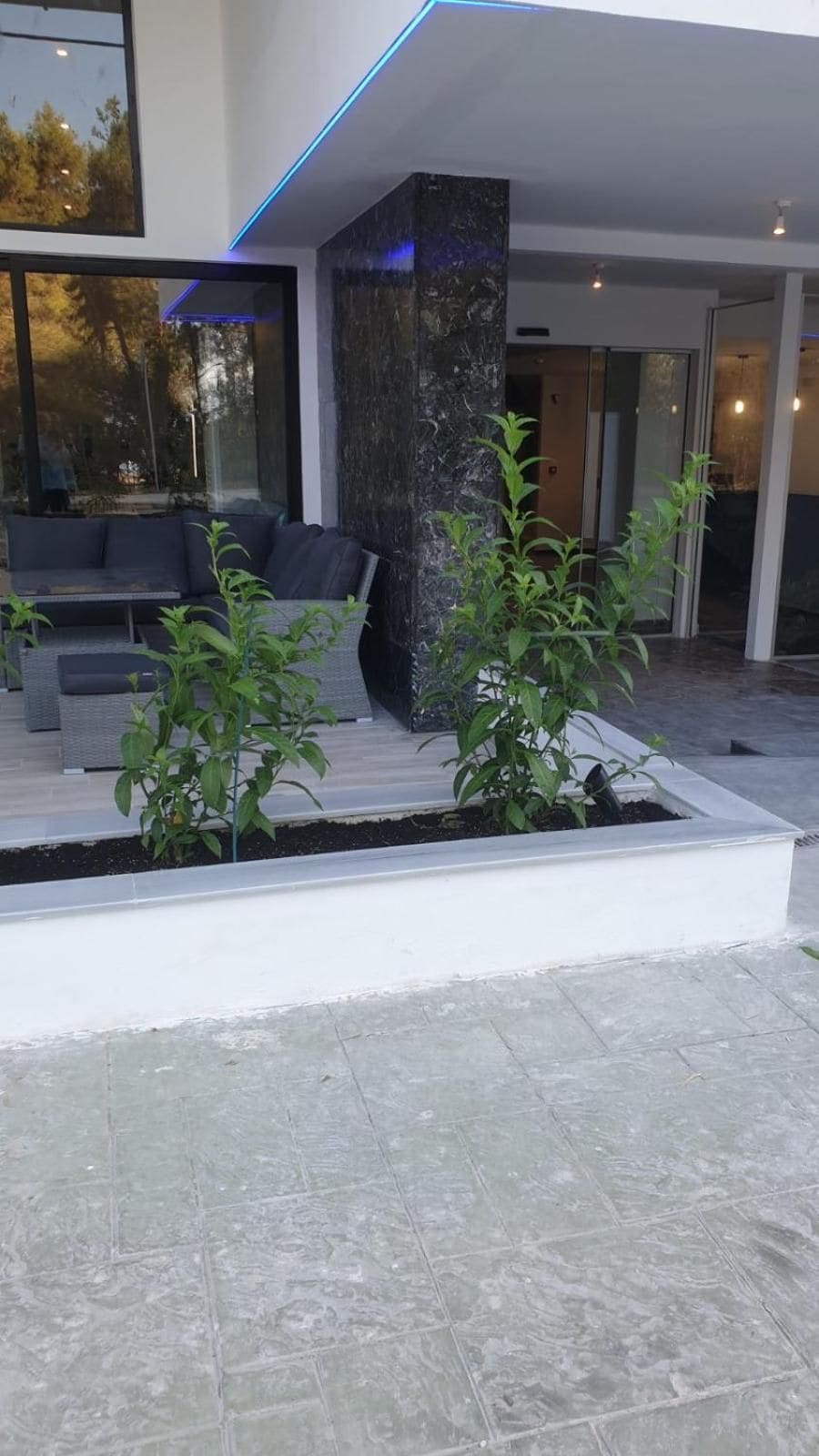 A modern outdoor seating area with a stone pillar, a sofa, and potted plants.