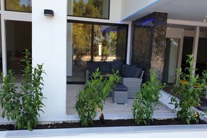A modern outdoor seating area with a sofa and cushions, surrounded by potted plants. - Evita Blue Hotel (Xylokastro-Evrostina)