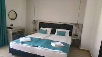 A double bed with a white and teal bedspread, two bedside tables with lamps, and a round mirror on the wall.