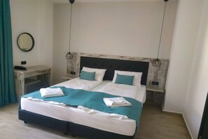 A double bed with a white and teal bedspread, two bedside tables with lamps, and a round mirror on the wall. - Evita Blue Hotel (Xylokastro-Evrostina)
