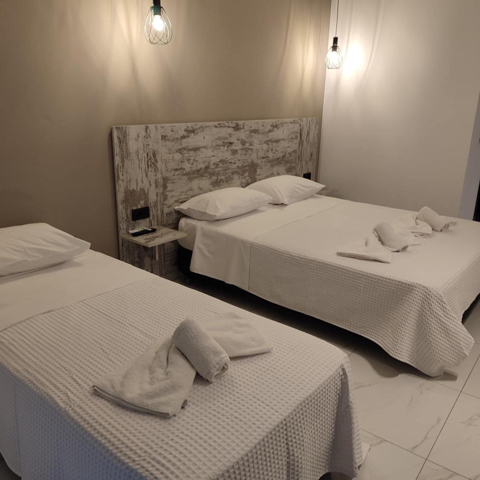 A hotel room with two beds, each with white linens and towels, a wooden headboard, and a nightstand with a remote control.