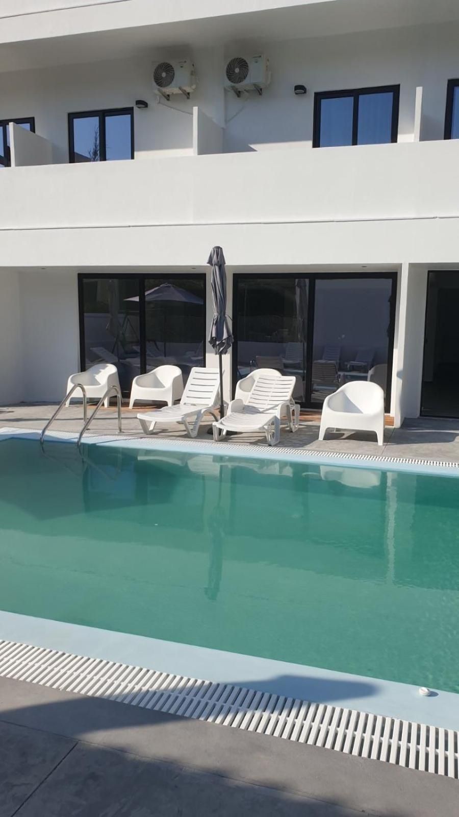Una piscina con sillas de descanso y una sombrilla, rodeada por un edificio con ventanas grandes y unidades de aire acondicionado.