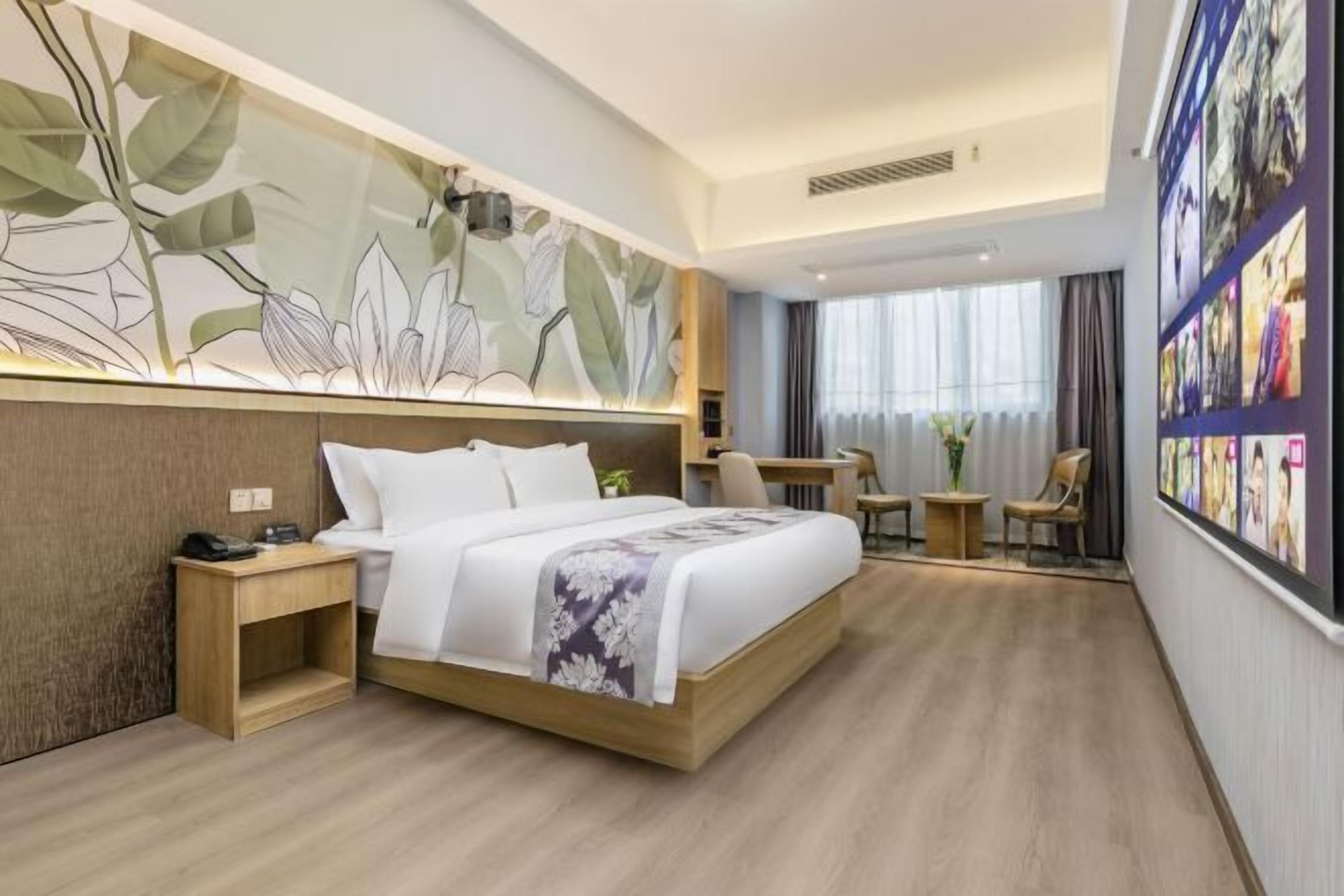 A modern hotel room with a large bed, a small desk, a chair, and a wall with framed pictures.
