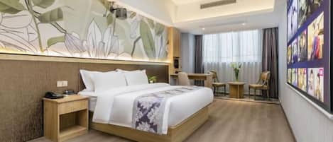A modern hotel room with a large bed, a small desk, a chair, and a wall with framed pictures.