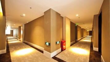 A hotel corridor with a carpeted floor, walls with a light color, and a red emergency exit sign.