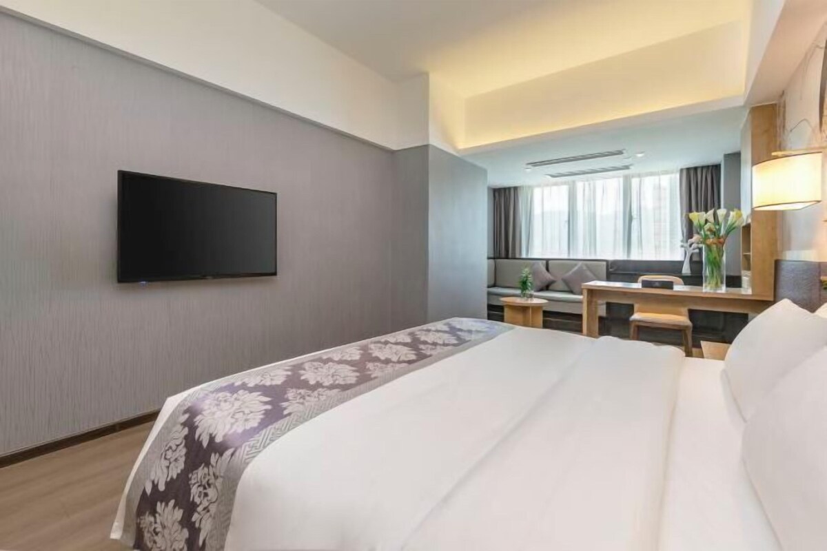 Habitación de hotel con cama, televisor de pantalla plana en la pared, escritorio con silla y ventana con cortinas.