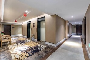 Un pasillo de hotel con piso alfombrado, un banco de madera y una puerta con adorno rojo.