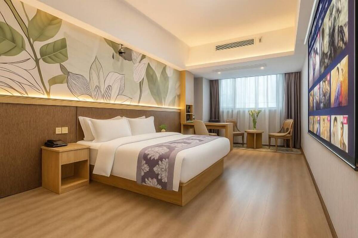 Habitació d'hotel amb llit, taulell de nit, làmpada, cadira, escriptori i una obra d'art a la paret.