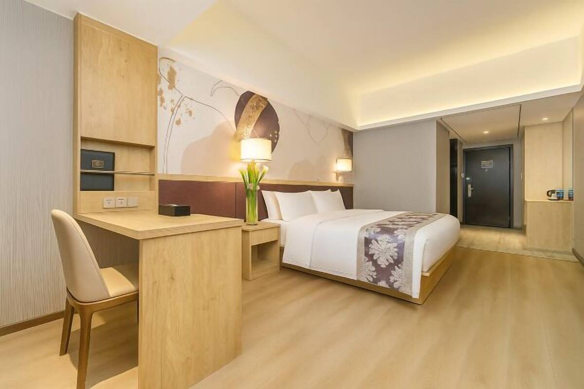 Habitació d'hotel amb llit, escriptori, cadira i un mur amb un disseny floral.