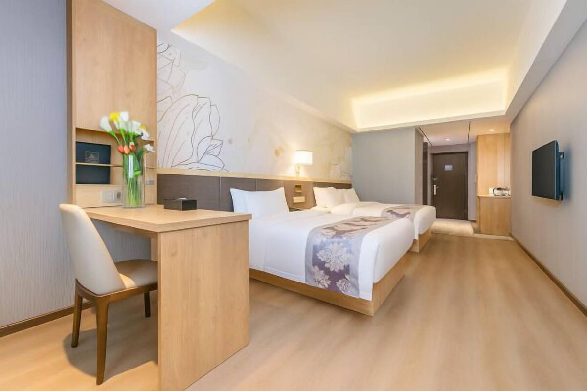 Una habitació d'hotel amb un llit, una taula de treball, una cadira, un televisor i una paret amb un dibuix lineal.