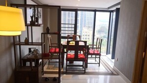 Un espace repas comprenant une table et des chaises, une lampe, et une vue sur les bâtiments à travers de grandes fenêtres.