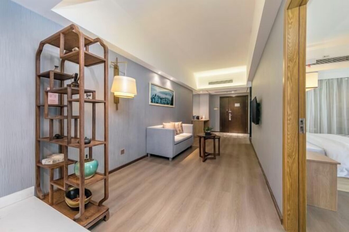Habitación de hotel con una estantería de madera, un sofá, una mesita y un televisor montado en la pared.